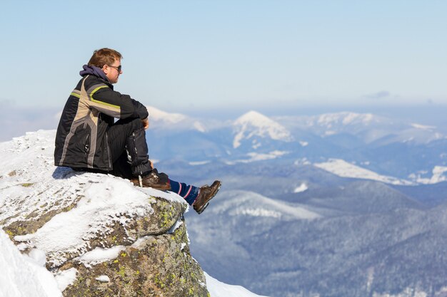 Turista che si siede sulla cima della montagna nevosa che gode della vista