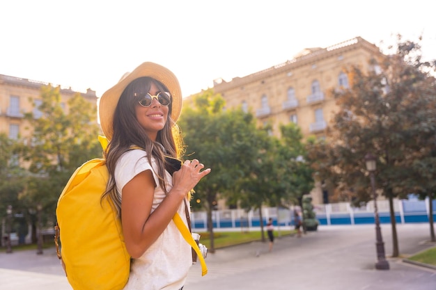 Turista con un cappello nel tramonto estivo accanto a una chiesa con una macchina fotografica cappello zaino giallo e occhiali da sole