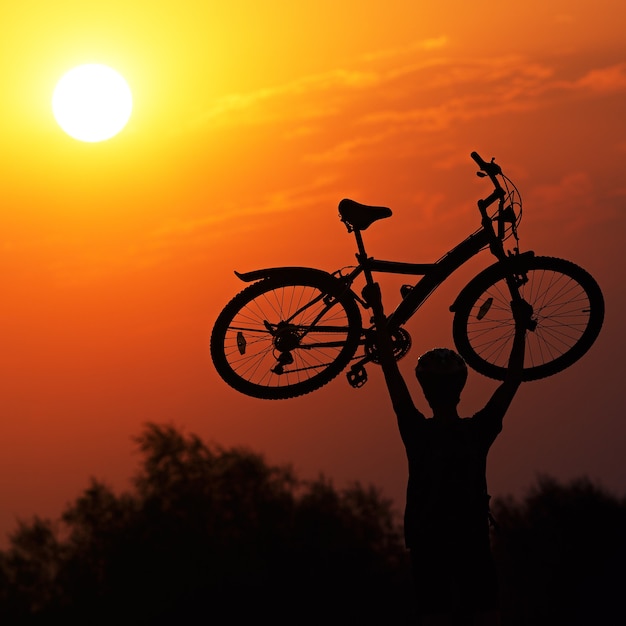 Turista con una bici sullo sfondo del tramonto.