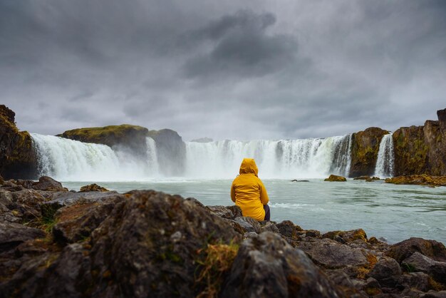 Turista con una giacca gialla che si rilassa alla cascata di Godafoss in Islanda