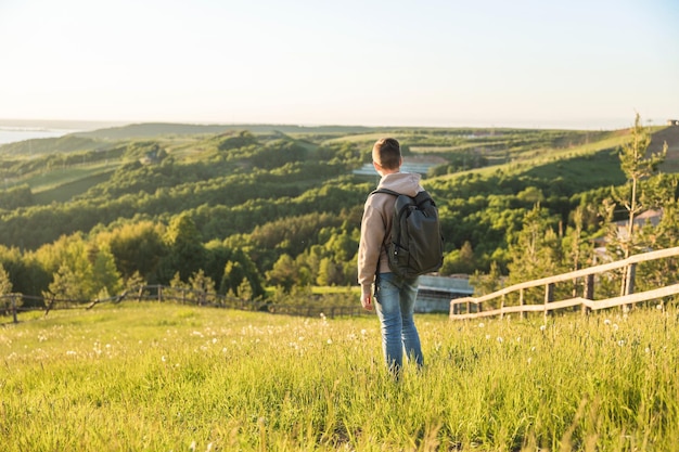 Turista con zaino in piedi sulla cima della collina nel campo in erba e godersi la splendida vista del paesaggio Vista posteriore dell'escursionista adolescente che riposa nella natura Stile di vita attivo Concetto di viaggio locale