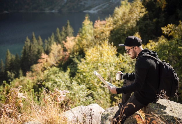 Turista dell'uomo che si rilassa sulla cima di una collina, guardando il meraviglioso scenario delle montagne e del lago.