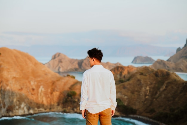 Turista dell'uomo in abito bianco in piedi sulla cima dell'isola di Padar con sfondo sfocato di mare e collina