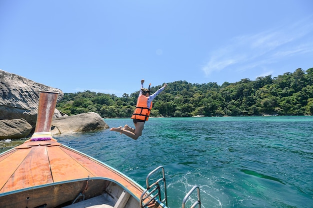 Turista della donna che salta sulla barca di legno nel mare tropicale