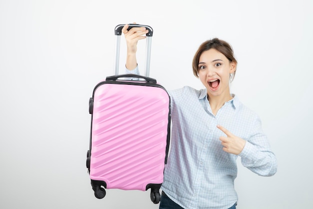 Turista della donna in piedi e indicando la valigia da viaggio rosa. Foto di alta qualità