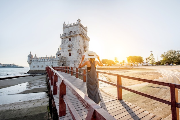 Turista della giovane donna che cammina sul ponte della torre di Belem sulla riva del fiume durante il tramonto a Lisbona, Portugal