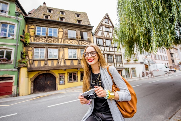 Turista della giovane donna che sta con la macchina fotografica della foto davanti alle belle case a graticcio che viaggiano nella città di Strasburgo, France