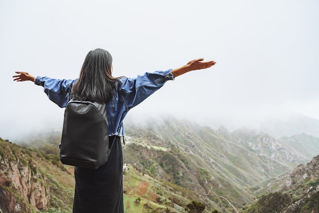 Turista della giovane donna con lo zaino che si rilassa sulla cima di una montagna e che gode della vista della valle