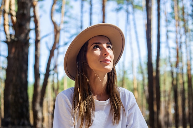 Turista della giovane donna in cappello e maglietta durante una sosta nella foresta.