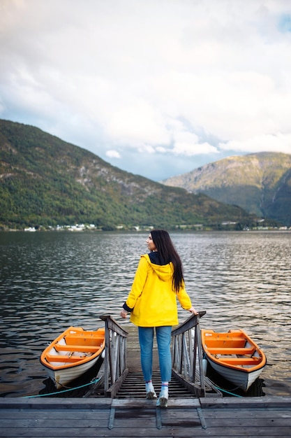 Turista della ragazza in una giacca gialla che posa sul lago in Norvegia Avventura di stile di vita itinerante