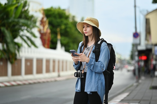 Turista di donna abbastanza caucasica in piedi nella strada trafficata della città a Chiang Mai nel nord della Thailandia e utilizzando smart phone