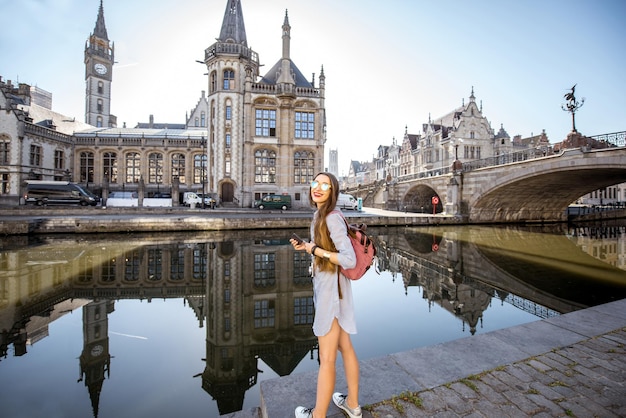 Turista di giovane donna che cammina con la macchina fotografica vicino al canale d'acqua con una splendida vista sulla città vecchia nella città di Gent in Belgio