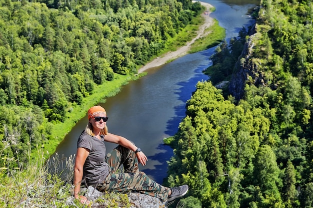 Turista escursionistico donna in bandana e occhiali da sole, che riposa sulla cima della montagna in una giornata di sole estivo.