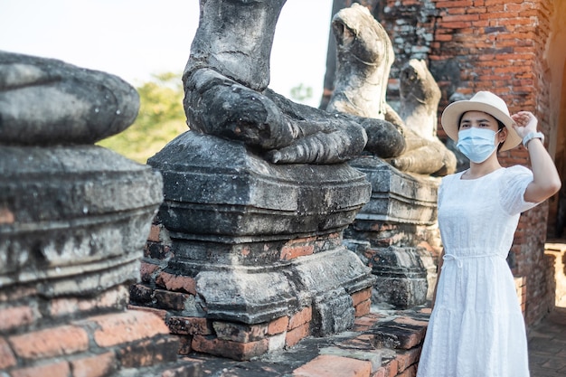 Turista femminile che indossa la mascherina chirurgica che visita il tempio di Wat Chaiwatthanaram