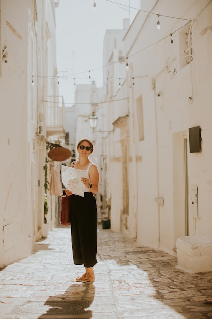 Turista femminile con una mappa cartacea della città sulle strade strette di Ostuni Italia