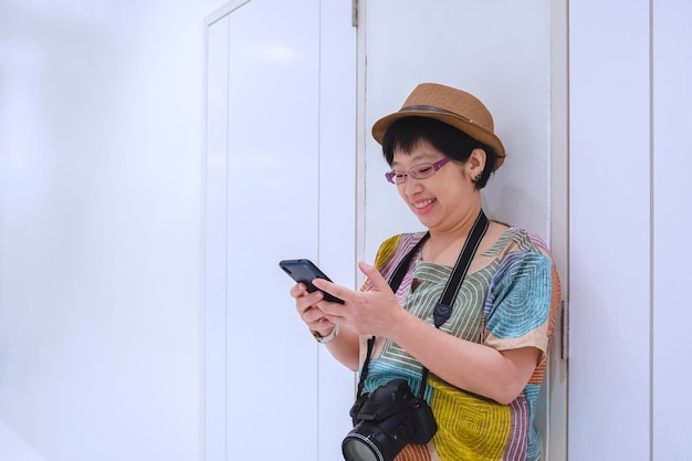 Turista femminile in stile vintage che utilizza lo smartphone mentre si trova sul muro bianco all'interno dell'edificio