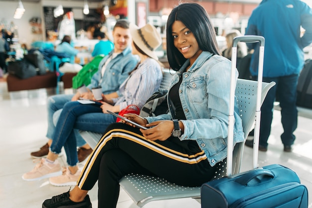 Turista femminile nero con la valigia in attesa della partenza in aeroporto.