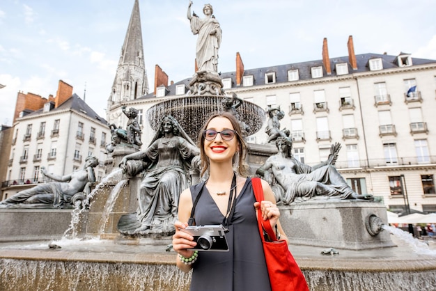 Turista giovane e felice con la macchina fotografica che sta vicino alla fontana sulla piazza reale nella città di Nantes, France