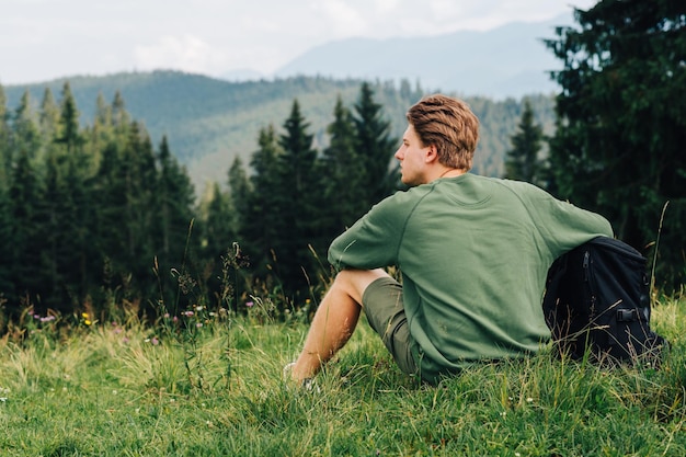 Turista hipster che riposa seduto su un prato in montagna che guarda lontano