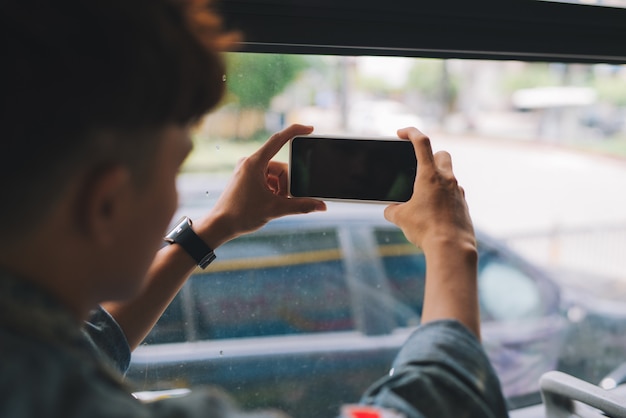 Turista maschio asiatico che fotografa la città dalla finestra del bus