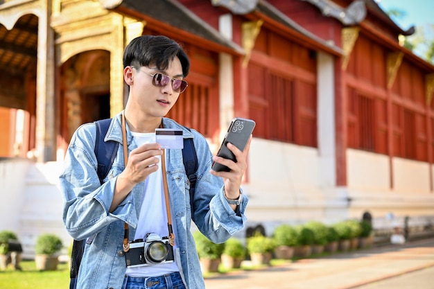 Turista maschio asiatico in possesso di uno smartphone e una carta di credito utilizzando la sua applicazione di mobile banking