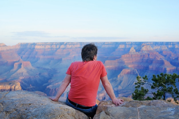 Turista maschio di mezza età che si siede sulla pietra e sullo sguardo del Grand Canyon da Mather Point