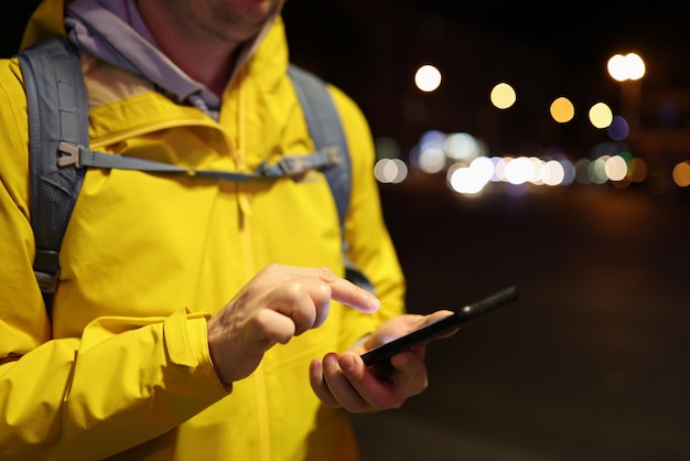 Turista maschio in cappotto giallo che utilizza il suo smartphone all'aperto