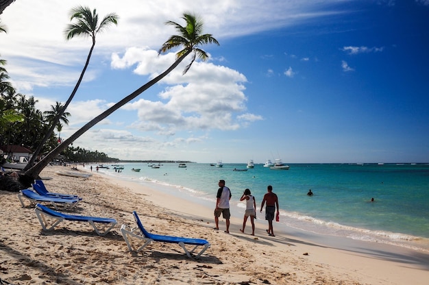 Turisti che camminano lungo la spiaggia con acque turchesi e alcune sedie a sdraio sulla sabbia a Punta Cana Repubblica Dominicana