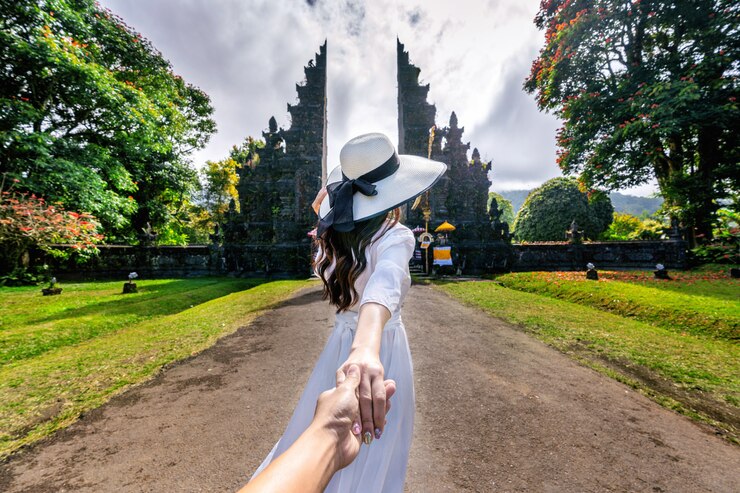 Turisti delle donne che tengono la mano dell'uomo e che lo conducono al grande portone in Bali, Indonesia.