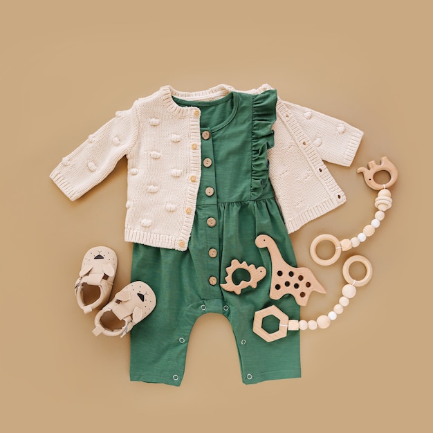 Tutina verde con maglione lavorato a maglia, giocattoli in legno e scarpe per bambini. Set di vestiti e accessori per bambini su fondo beige. Moda neonato. Disposizione piatta, vista dall'alto