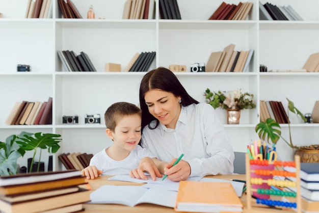 Tutor privato femminile che aiuta il giovane studente con i compiti alla scrivania nella stanza del bambino luminoso