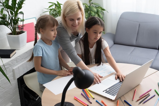 Tutore donna o madre adottiva che aiuta una ragazza caucasica carina a fare i compiti seduta al tavolo. Tata e bambino diversi che imparano a scrivere sul taccuino che studiano a casa.