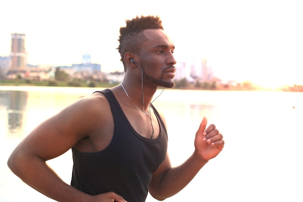 Tutta la lunghezza del giovane africano in abbigliamento sportivo che fa jogging mentre si allena all'aperto, al tramonto o all'alba. Corridore.