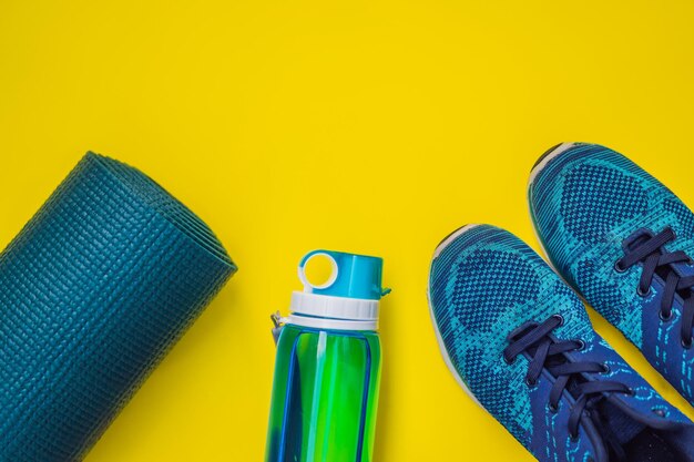 Tutto per lo sport sfumature blu turchese su sfondo giallo Tappetino da yoga scarpe sportive abbigliamento sportivo e bottiglia d'acqua Concetto stile di vita sano sport e dieta Attrezzature sportive Copia spazio