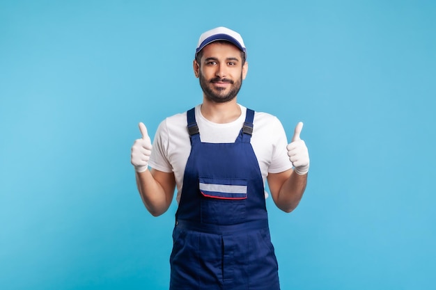 Tuttofare felice e soddisfatto in tuta e guanti per l'igiene che mostra i pollici in su, professione del settore dei servizi, consegna tramite corriere, manutenzione delle pulizie. Operaio in uniforme che gesticola come. girato in studio