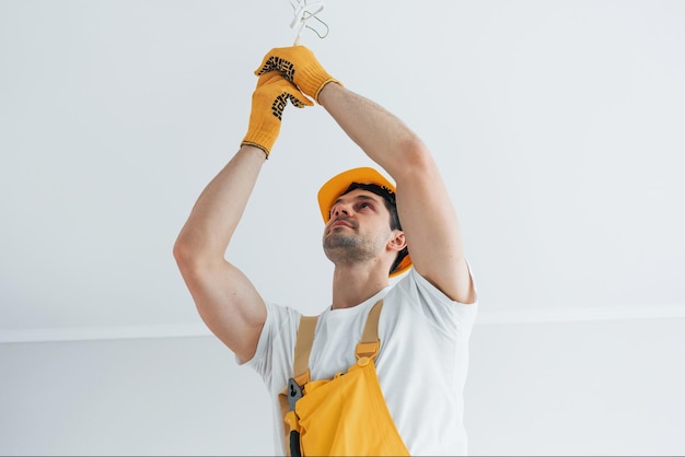 Tuttofare in uniforme gialla che cambia lampadina Concezione di ristrutturazione della casa