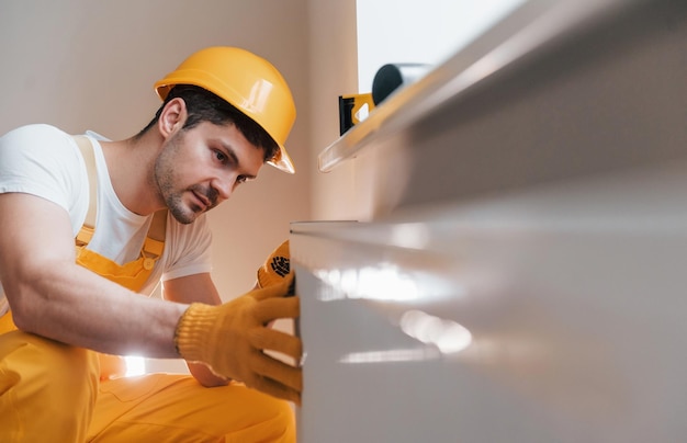 Tuttofare in uniforme gialla che installa una nuova batteria Concezione di ristrutturazione della casa