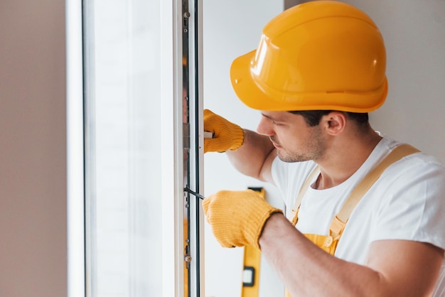 Tuttofare in uniforme gialla installa una nuova finestra Concezione di ristrutturazione della casa