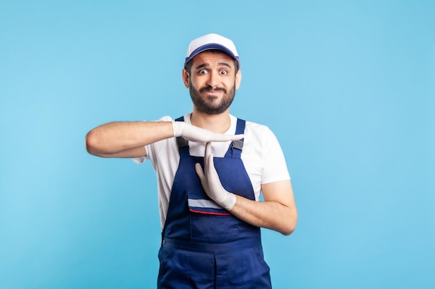 Tuttofare oberato di lavoro in tuta e guanti che mostra un gesto di timeout, ha bisogno di una pausa. Professione nel settore dei servizi, consegna tramite corriere, manutenzione delle pulizie. Operaio in uniforme gesturing stop. isolato