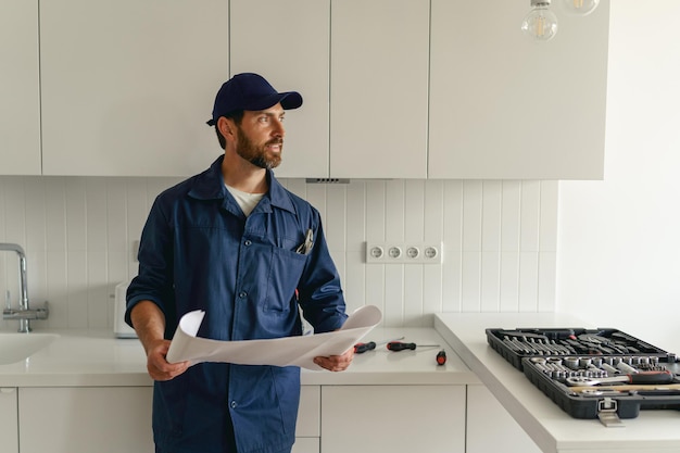 Tuttofare professionista in uniforme in piedi sulla cucina con piano casa e cassetta degli attrezzi prima di iniziare il lavoro