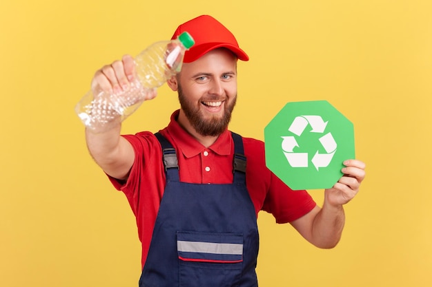 Tuttofare sorridente in piedi e con in mano un cartello di riciclaggio e una bottiglia di plastica che pensa in verde