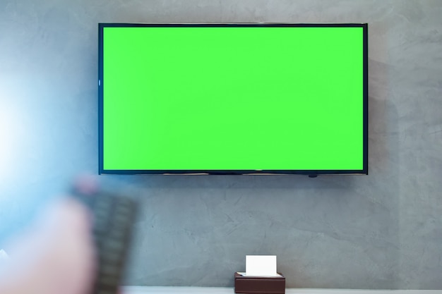 TV a LED con schermo verde sul muro in camera moderna con telecomando sfocato