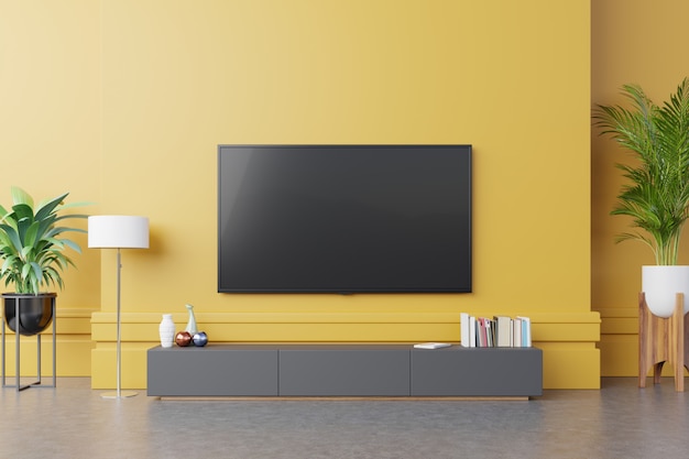 TV sul mobile in soggiorno moderno con lampada, tavolo, fiori e piante su sfondo giallo muro.