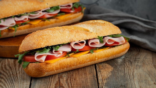Two Long baguette Sandwiches with arugula slices of fresh tomatoes ham and cheese