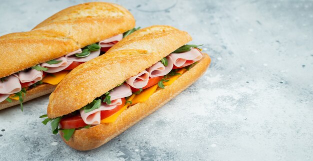 Two Long baguette Sandwiches with ham and cheese.