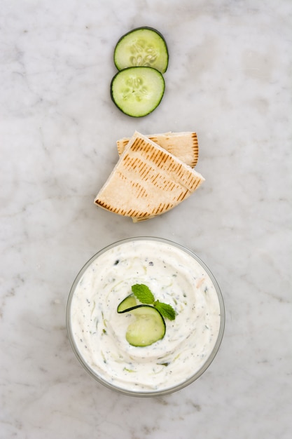 Tzatziki in ciotola e ingredienti su marmo bianco