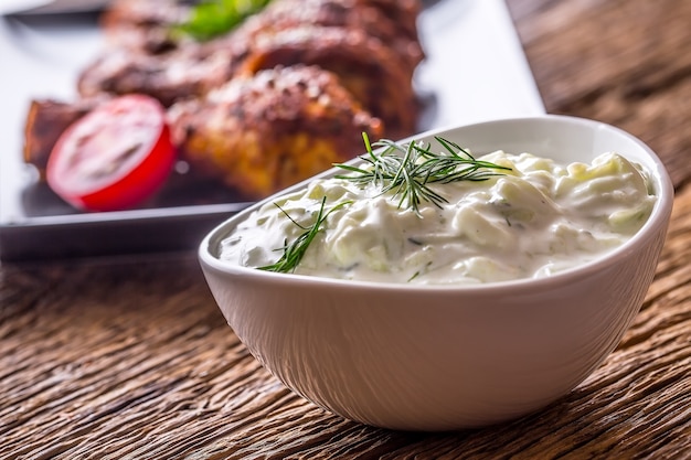 Tzatziki. Salsa Tzatziki o condimento con cosce di pollo alla griglia in sottofondo.