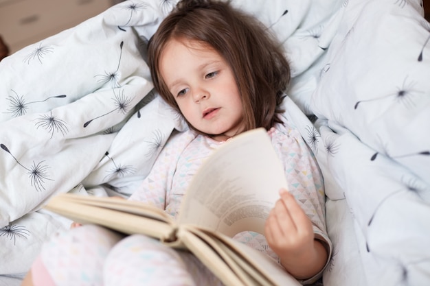 Ubicazione sveglia del libro di lettura della ragazza nel suo letto e legge le fiabe interessanti