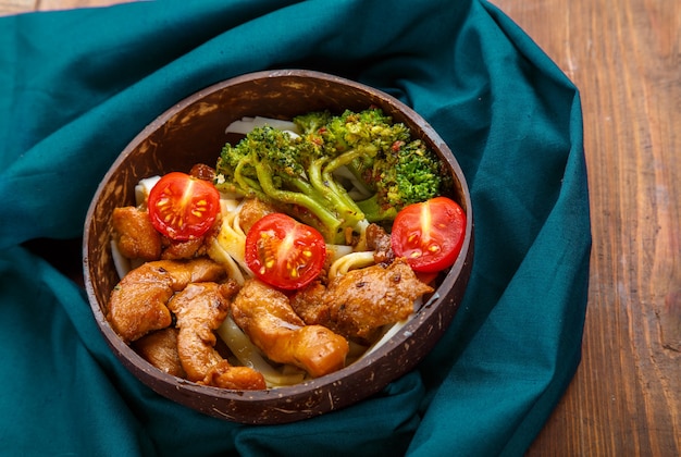 Udon con carne e verdure in salsa yakiniku in un piatto di gusci di cocco su un tavolo di legno su un tovagliolo blu. Foto orizzontale