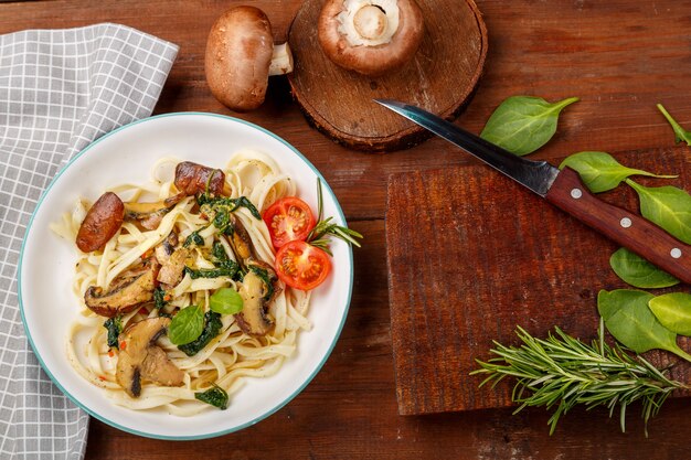 Udon con funghi e spinaci in un piatto su un tovagliolo grigio accanto a un coltello e funghi e verdure sul tagliere